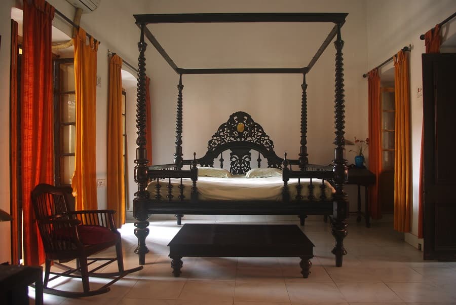 <p><em>A traditional four-poster bed and armchair in a room at the Itachuna Rajbari (Picture by Amitabha Gupta, Wikimedia Commons)</em></p>
