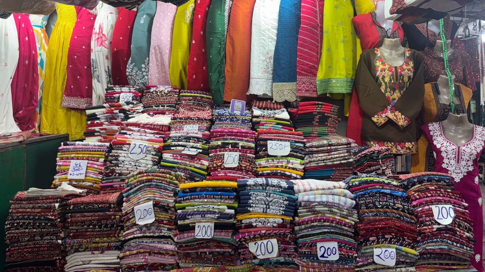 <p>Towers of printed kurtis are stacked with their prices scribbled by hand. &nbsp;</p>
