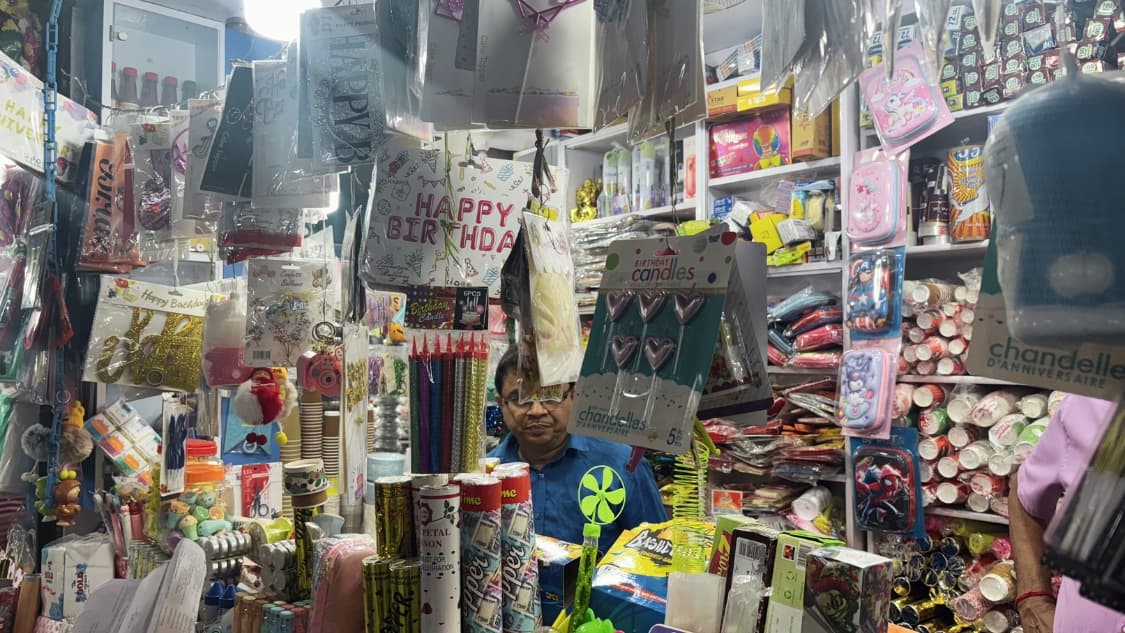 <p>A bustling stall packed with birthday celebration essentials, including "Happy Birthday" banners, heart-shaped candles, party poppers and character-themed stationery sets.</p>