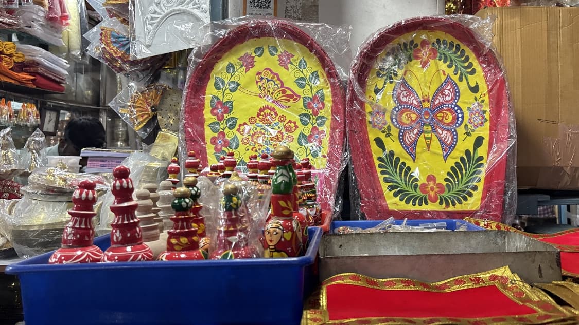 <p>A display of traditional Bengali wedding and ritual items including brightly painted kulas (winnowing fans) adorned with butterfly motifs.</p>