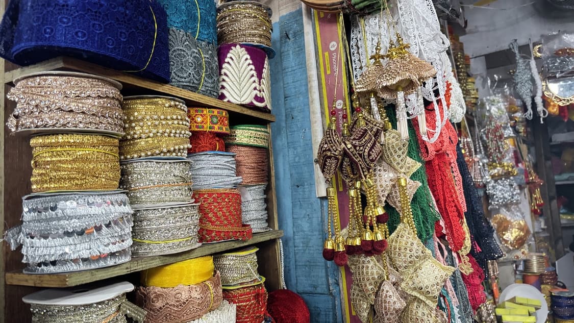 <p>Rolls of embroidered trims and ornate tassels spill from a shop that supplies fabrics and embellishments for weddings, festivals and tailoring.</p>