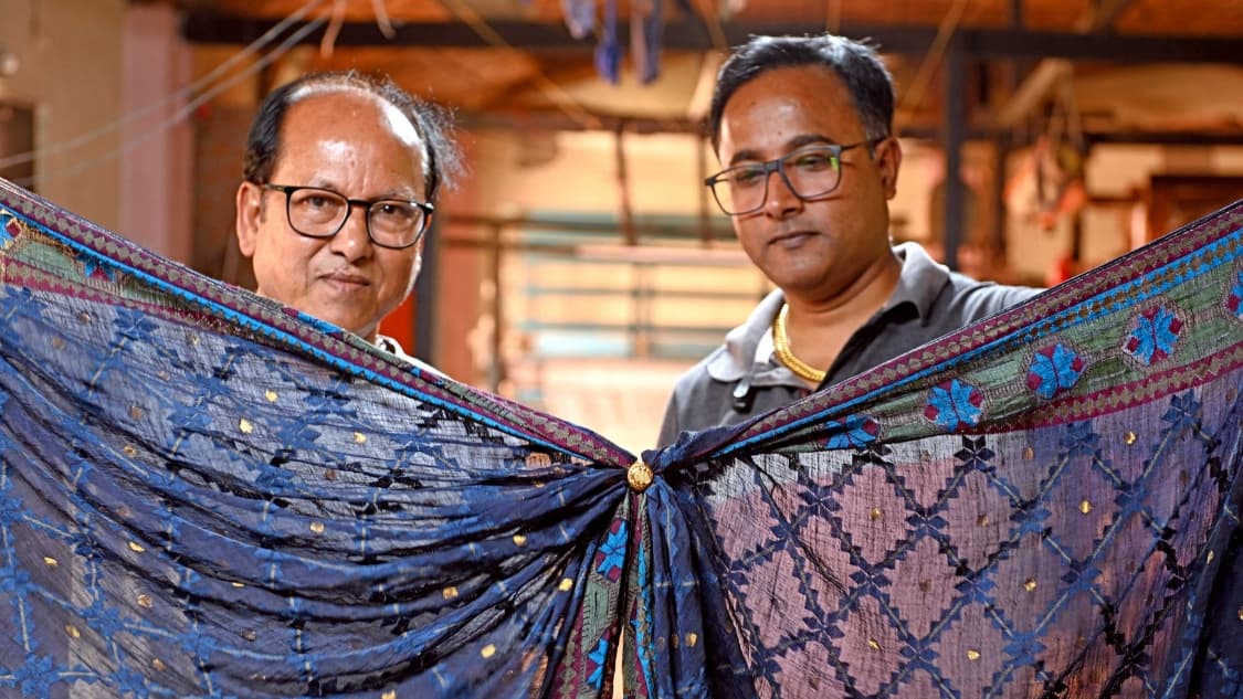 <p>Padma Shri awardee Jyotish Debnath of Kalna, pictured with his son Rajib holding a muslin sari and ring, explains that an authentic muslin sari is so fine it can pass effortlessly through a finger ring without snagging.</p><p>&nbsp;</p>