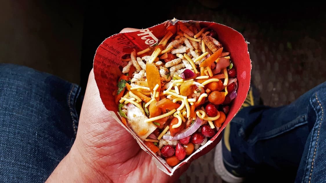 <p>A passenger enjoying jhalmuri during a local train journey. (Picture by Ajaybiswas22, Wikimedia Commons)</p>